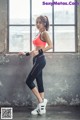 A woman in a red sports bra top and black leggings posing by a window.