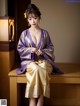 A woman in a purple kimono sitting on a wooden bench.