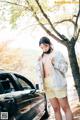 A woman standing next to a black car on a road.