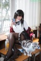 A woman sitting at a desk with a cat and a cell phone.